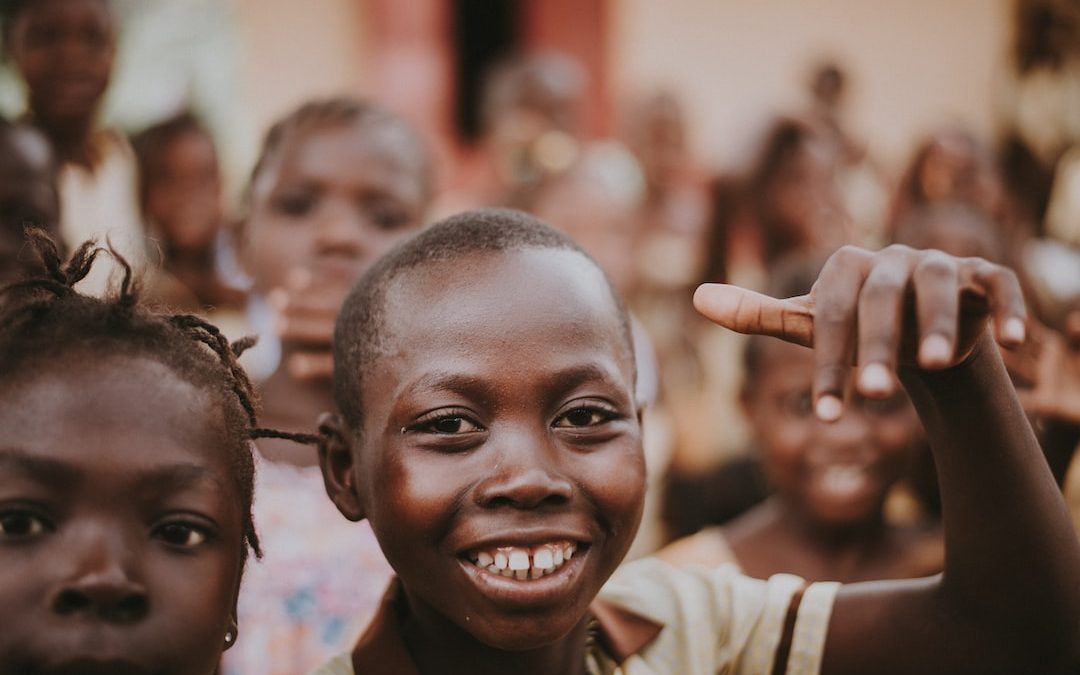 boy in brown collared top smiling and surrounded by children