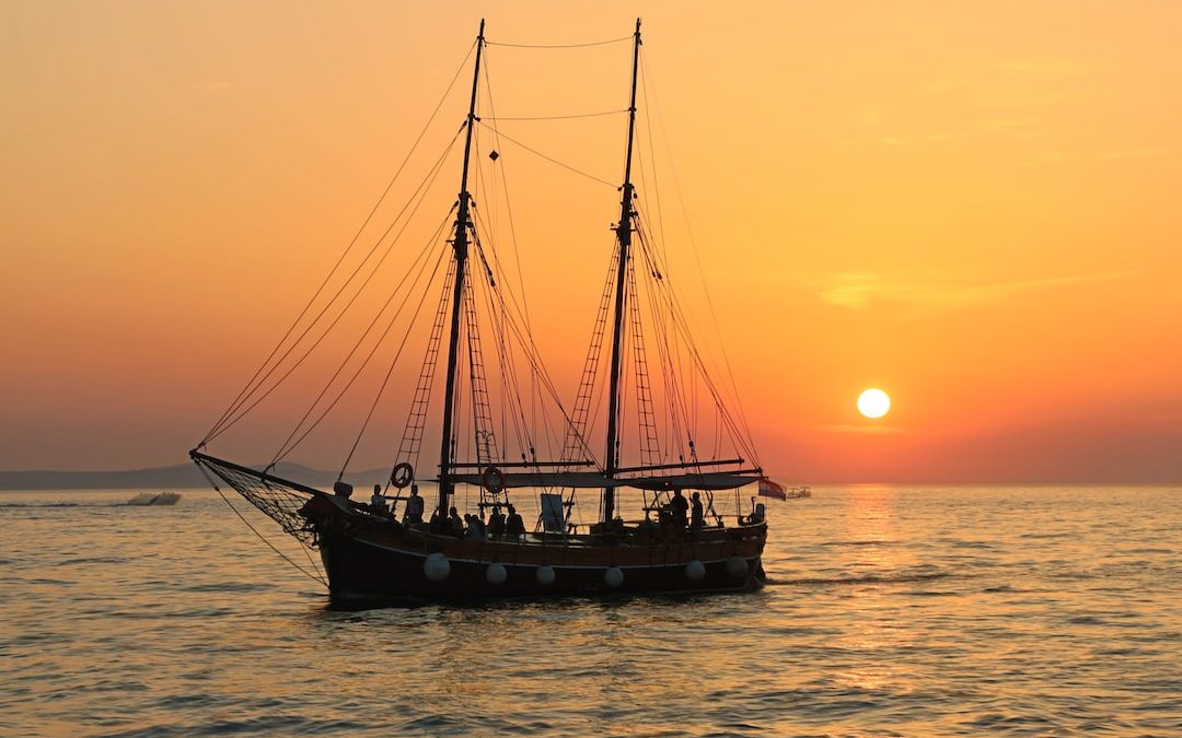 black and white sailboat in body of water during sunset