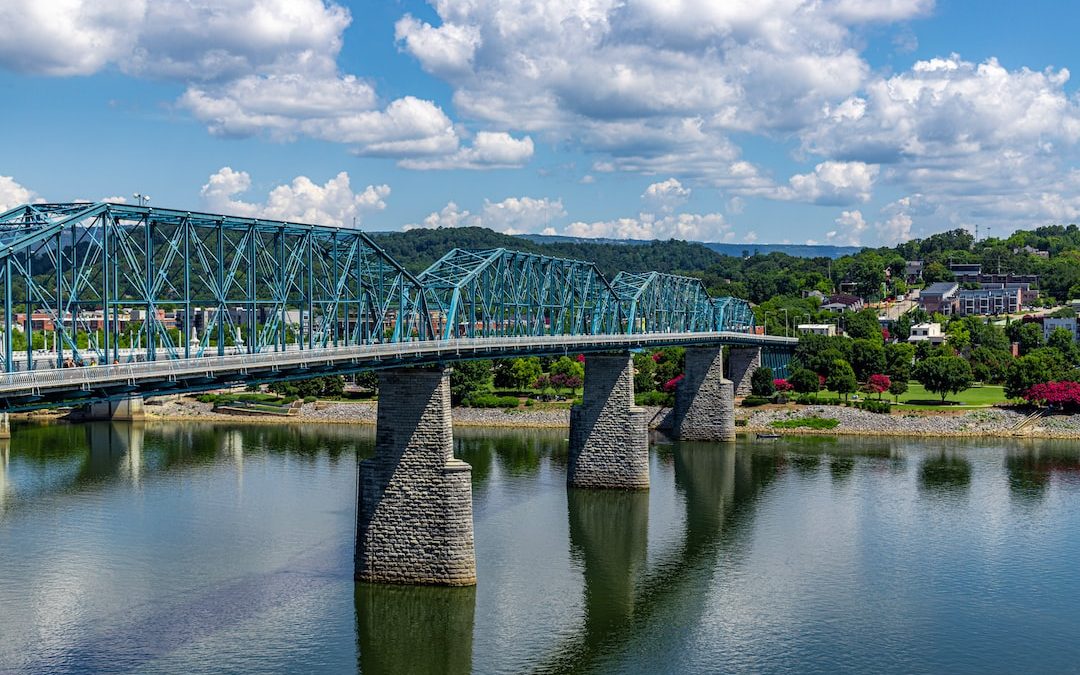 green metal bridge over river under blue sky and white clouds during daytime