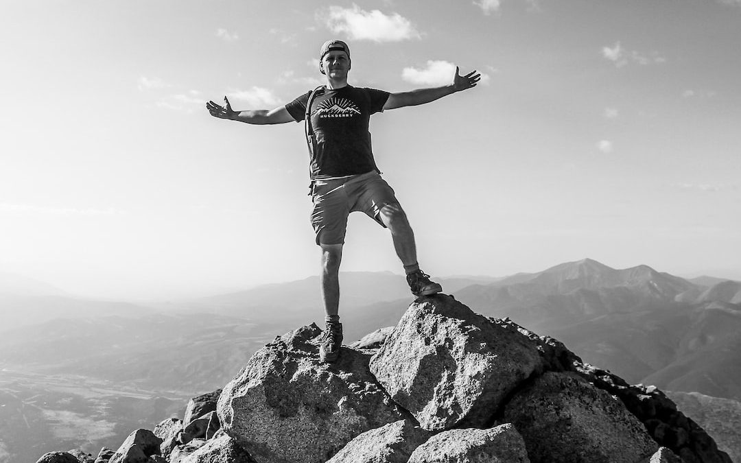 man in black tank top and white shorts standing on rock formation during daytime