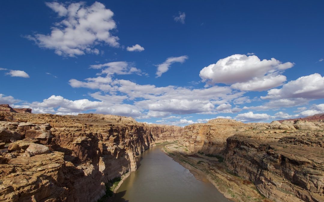 brown rocky mountain beside river under blue sky and white clouds during daytime