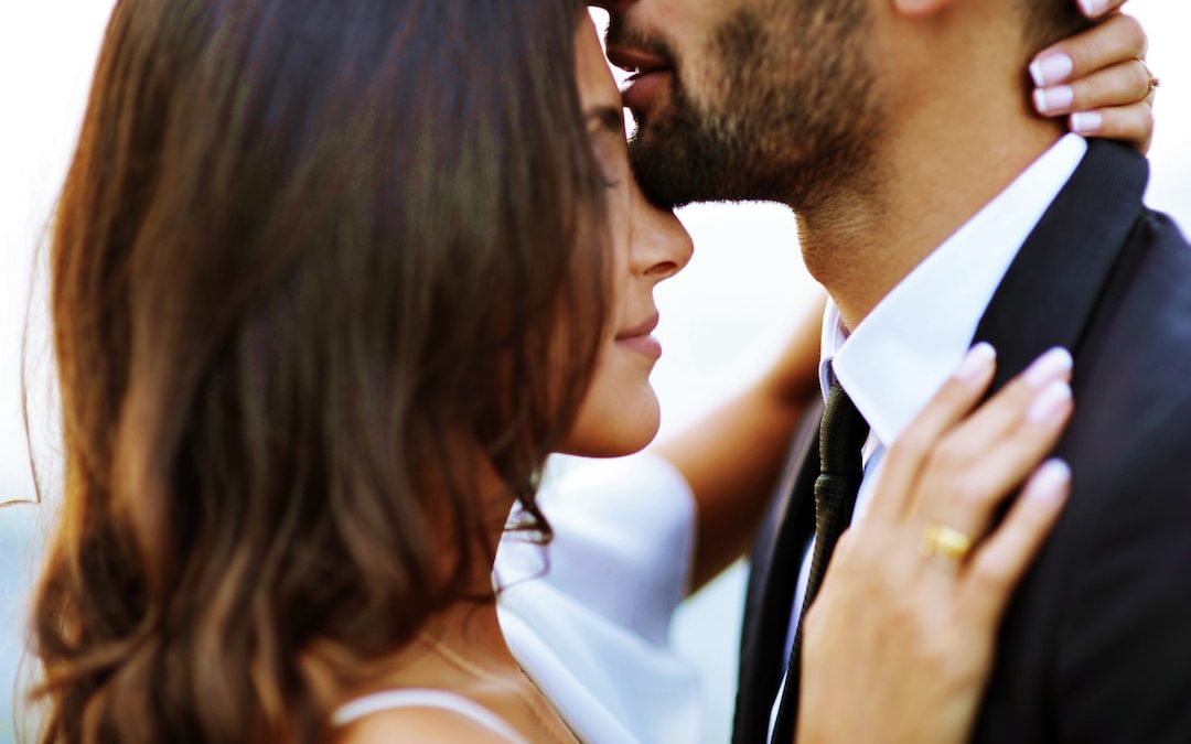 man kissing woman on her forehead