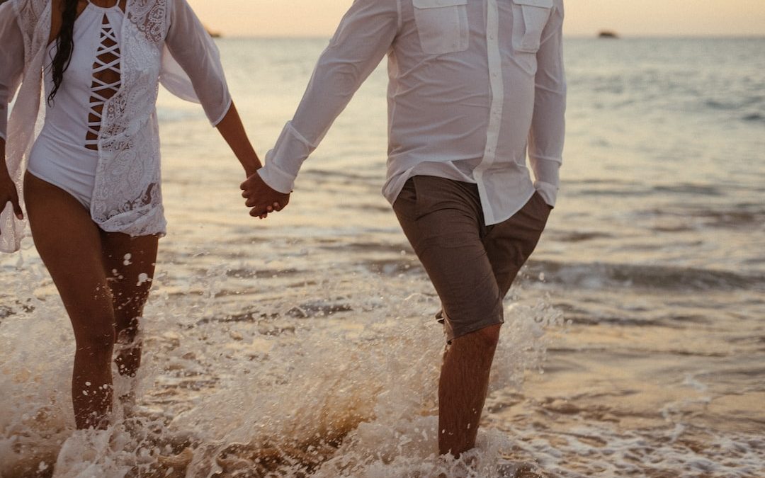 couple holding hands walking on shore