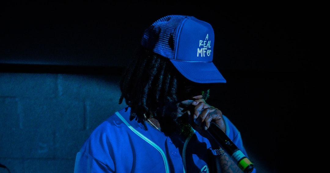 a man with dreadlocks and a blue hat singing into a microphone