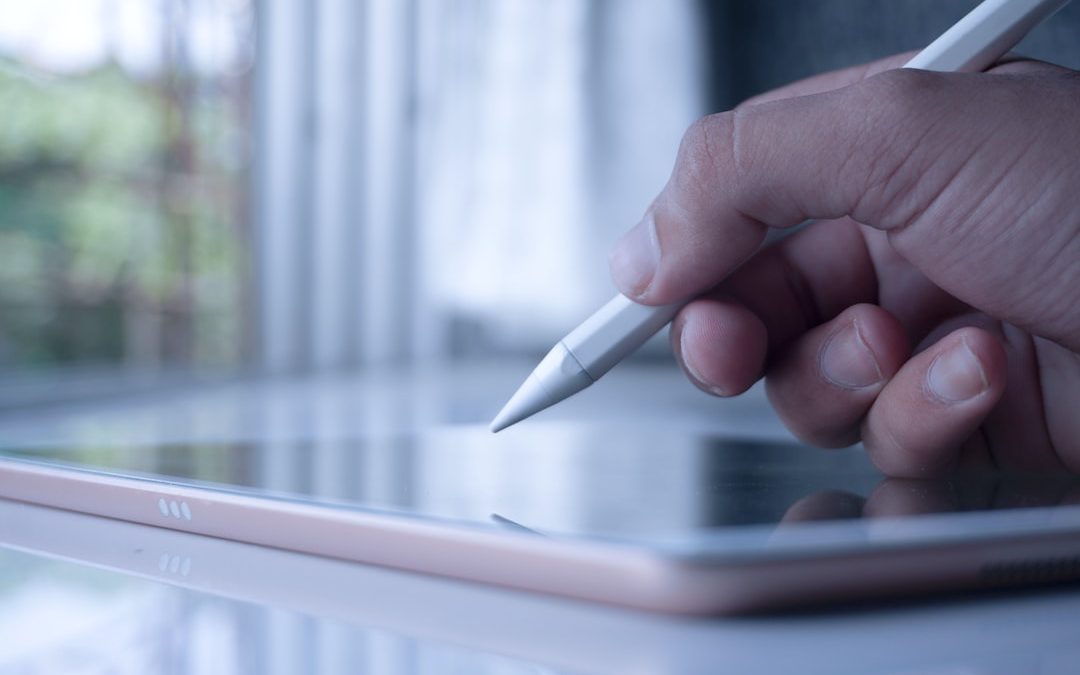 a person holding a pen and writing on a tablet