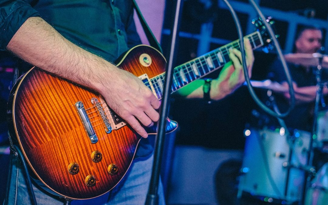 man standing and playing electric guitar near another man playing drums