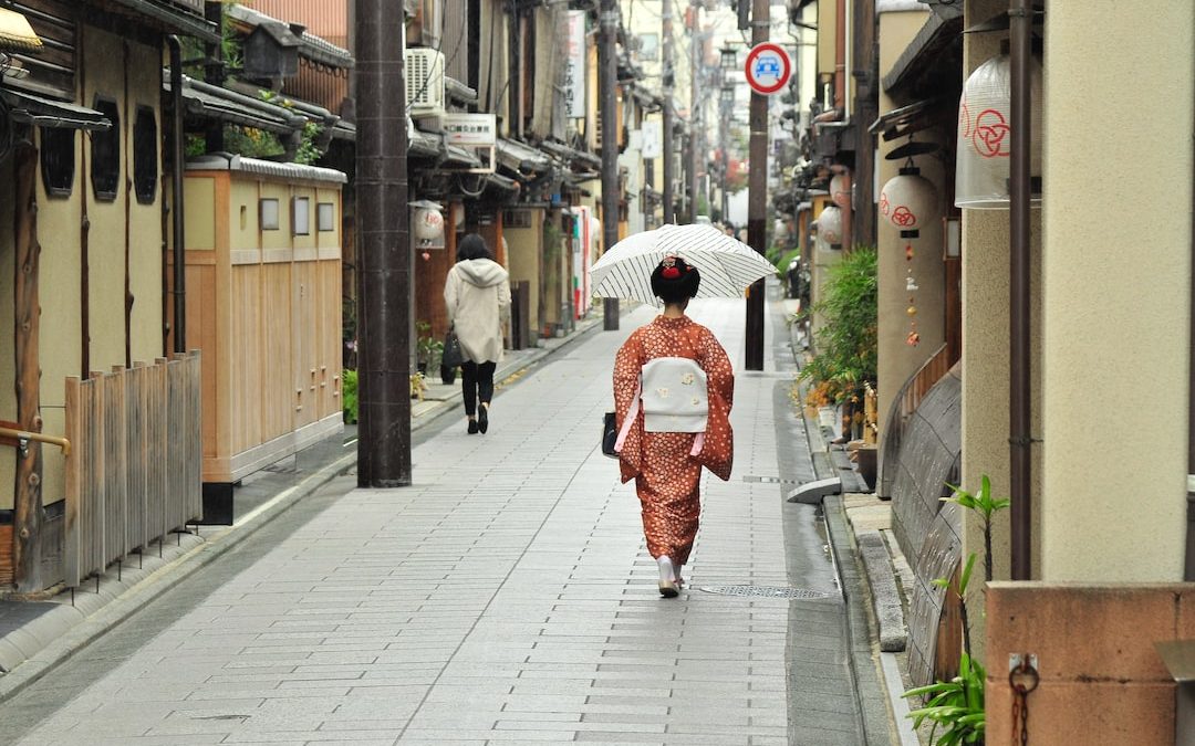 woman in red kimono holding umbrella walking on sidewalk during daytime