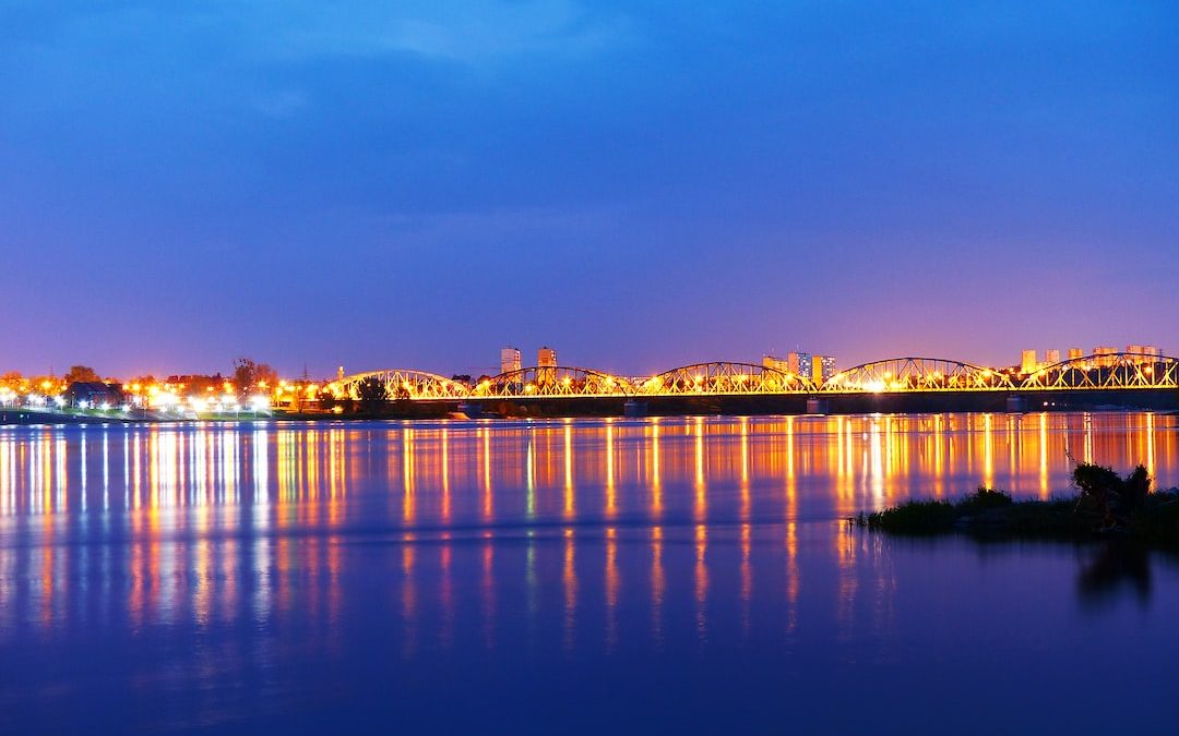 lighted bridge reflects on calm body of water under blue sky