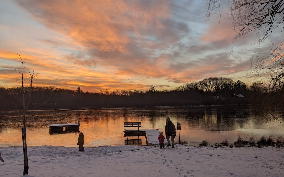 a group of people standing on a snowy field by a lake