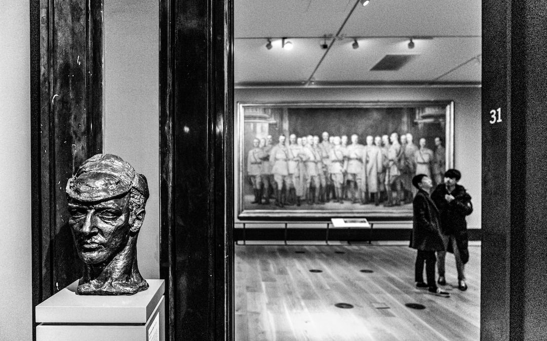 grayscale photo of man in black jacket standing near glass window