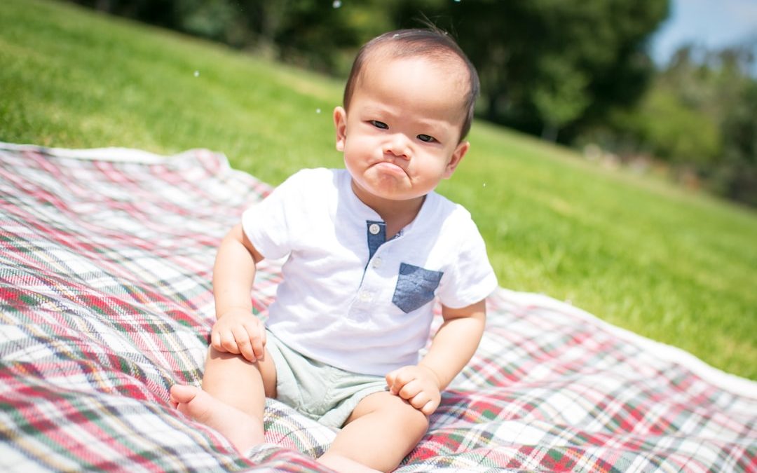 selective focus photography of grumpy face toddler sitting on plaid pad taken during daytime