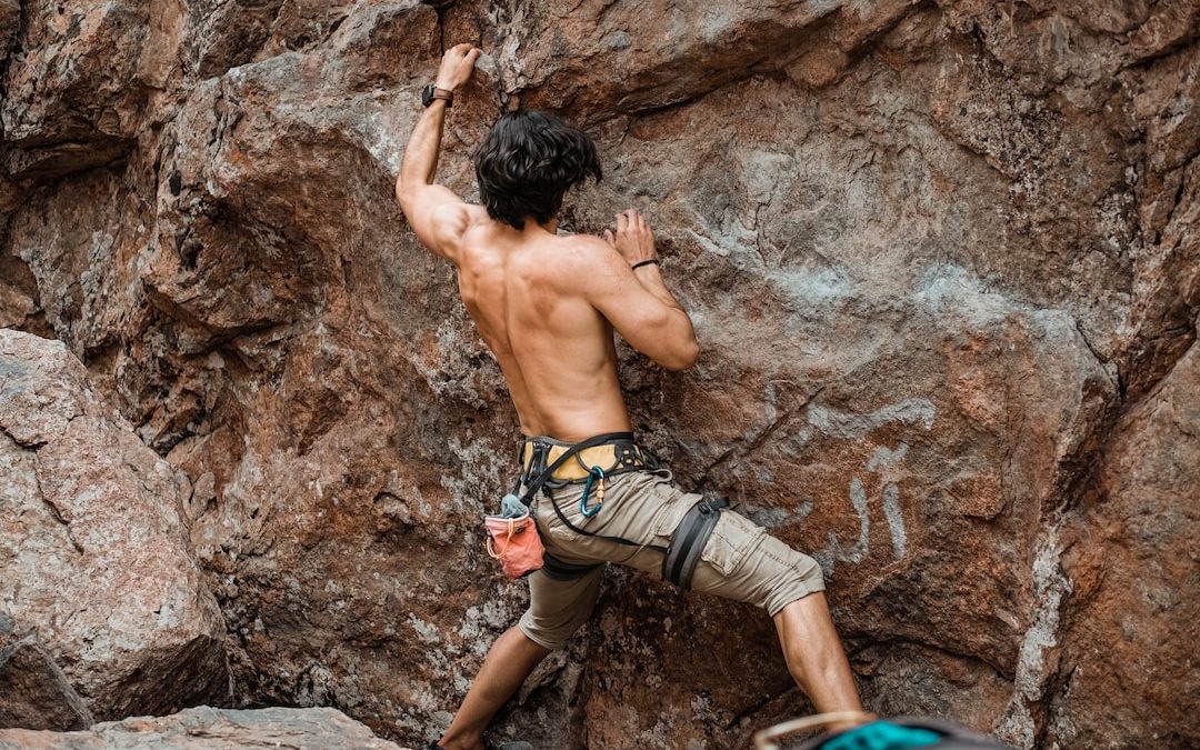 topless man climbing on brown rock formation during daytime