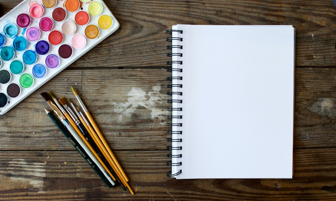 paint brushes next to drawing book and water color palette