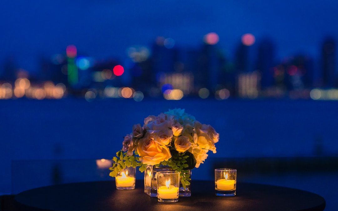 white rose bouquet in vase with three tealight candle votives on round brown wooden table