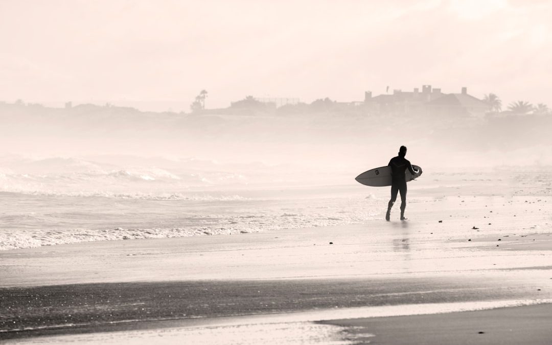 silhouette person walking on sandbank while holding surfboard