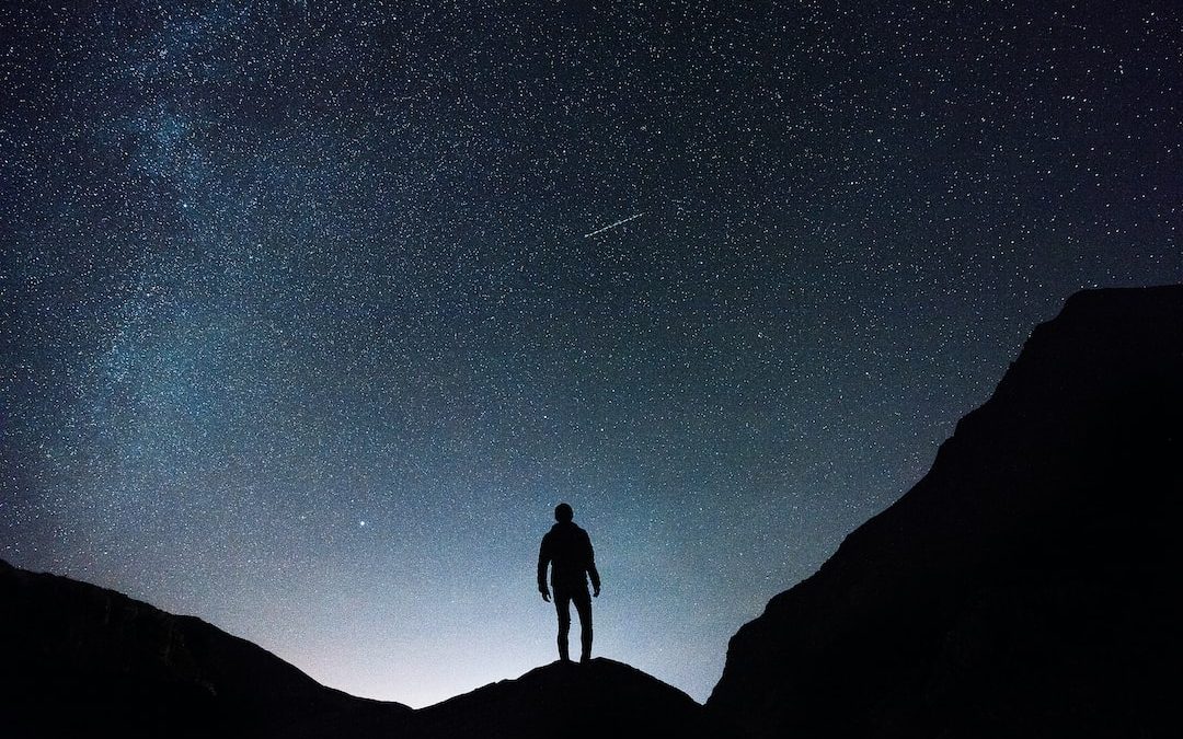 silhouette of man standing on hill during starry night