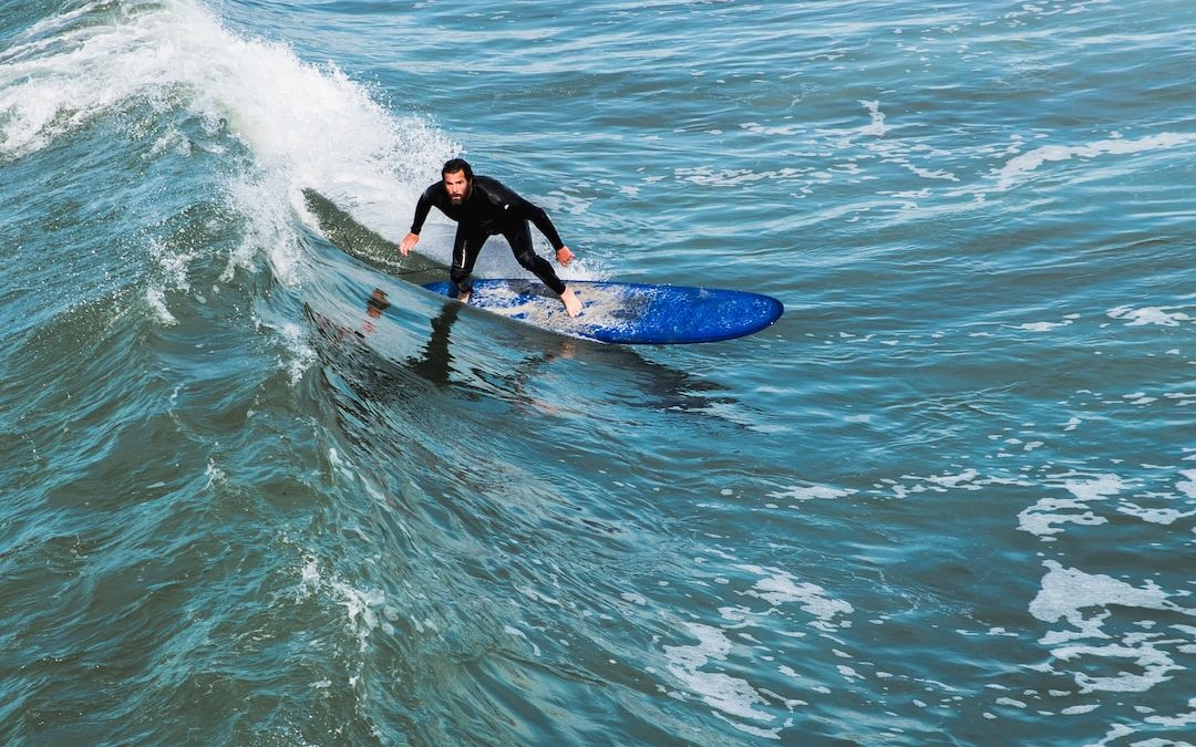 man in black wet suit surfing on wave during daytime