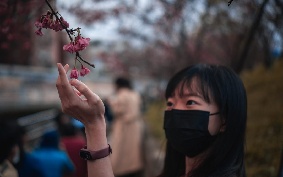 girl in black mask holding pink flower during daytime