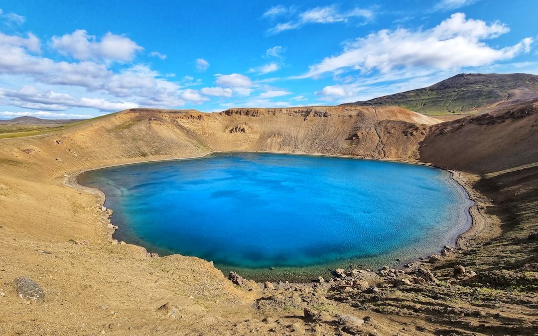 blue lake surrounded by brown and green mountains under blue sky during daytime