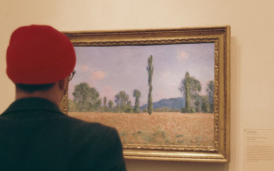 a man in a red hat looking at a painting