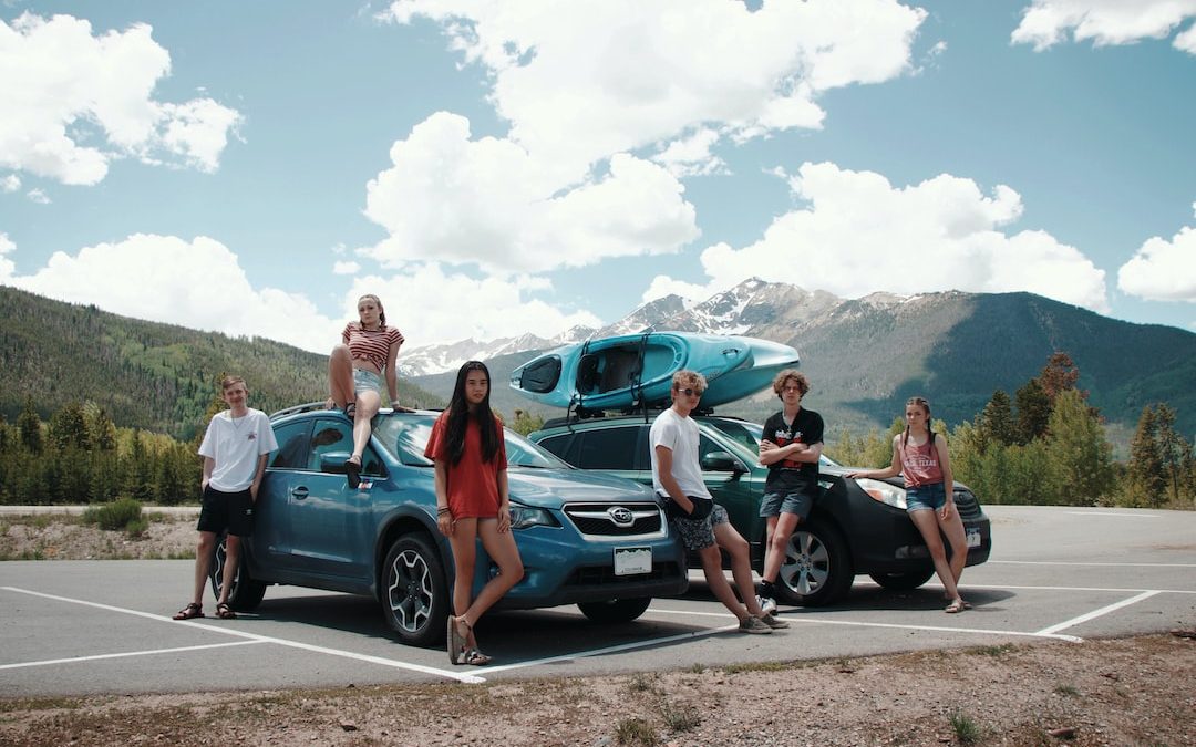 group of people standing beside blue car during daytime