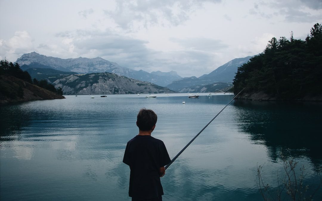 boy fishing on calm water at daytime