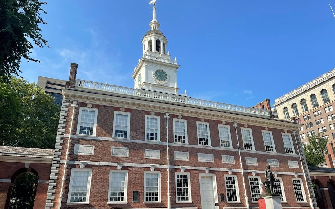 a large brick building with a clock tower with Independence Hall in the background
