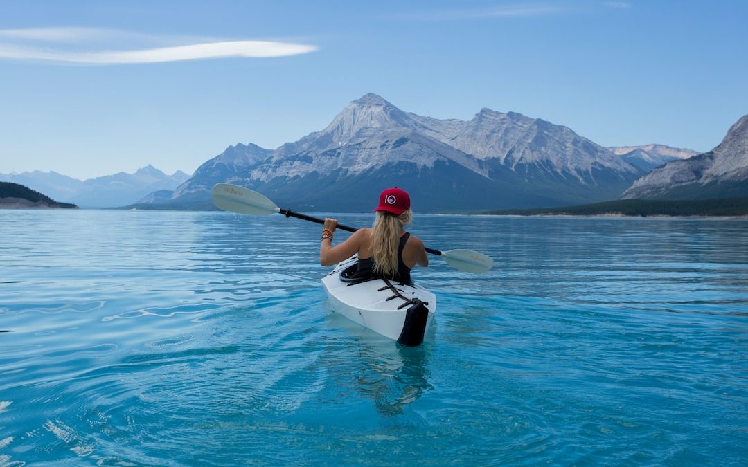 woman wearing red hat riding on white kayak facing mountain alps