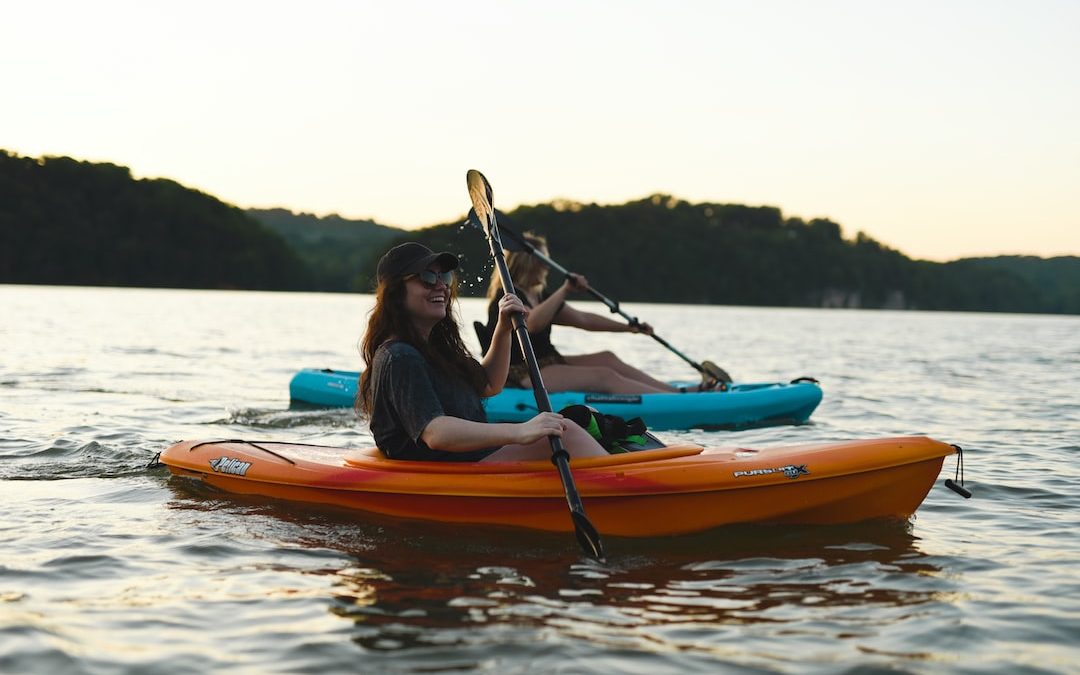 woman in blue shirt and blue denim jeans riding orange kayak on water during daytime