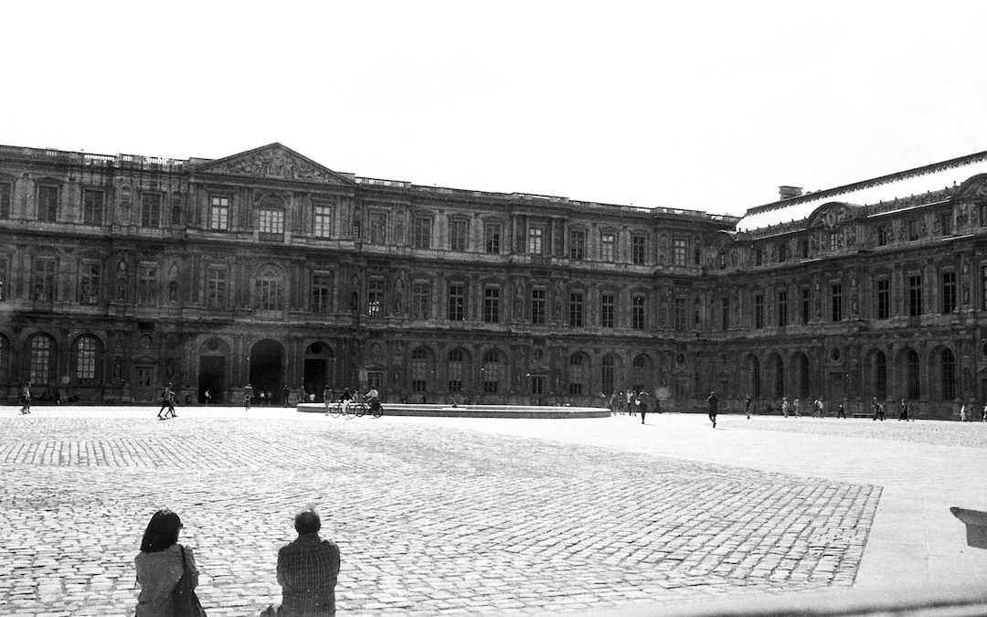 two people sitting on the ground in front of a large building