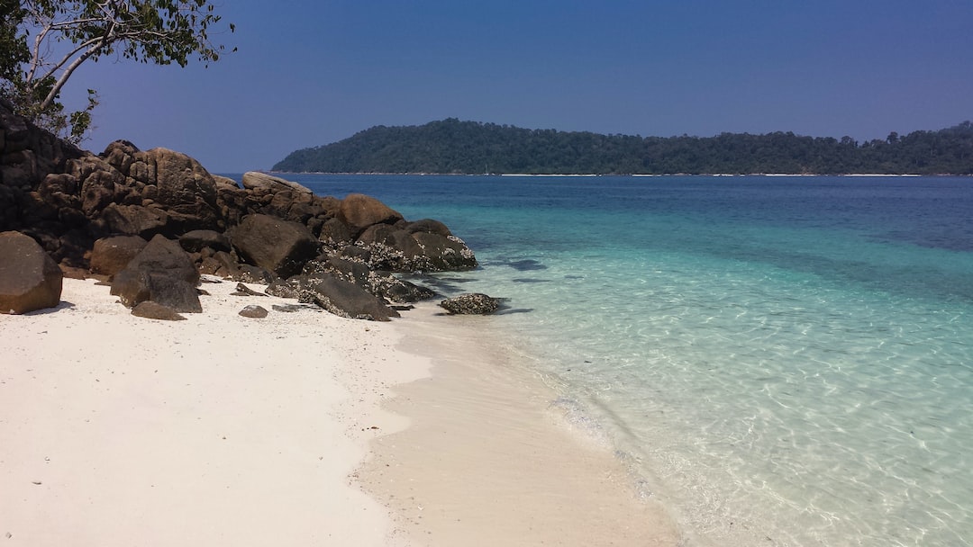 a sandy beach with clear blue water and rocks