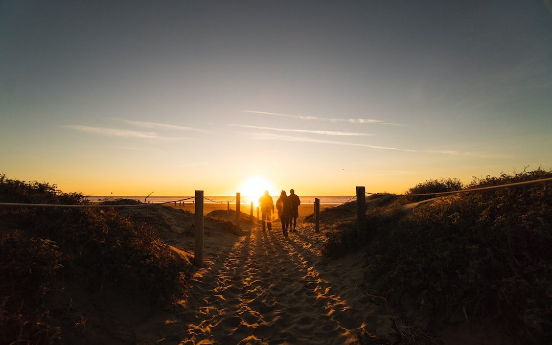 three person walking on sand dunes near beach