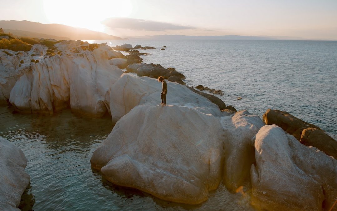 photo of person standing on brown boulder surrounded by water